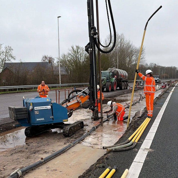 Mitarbeiter in orangefarbener Sicherheitskleidung führen mit einem blauen Bohrgerät Grundwasserabsenkungsarbeiten entlang einer Autobahn durch